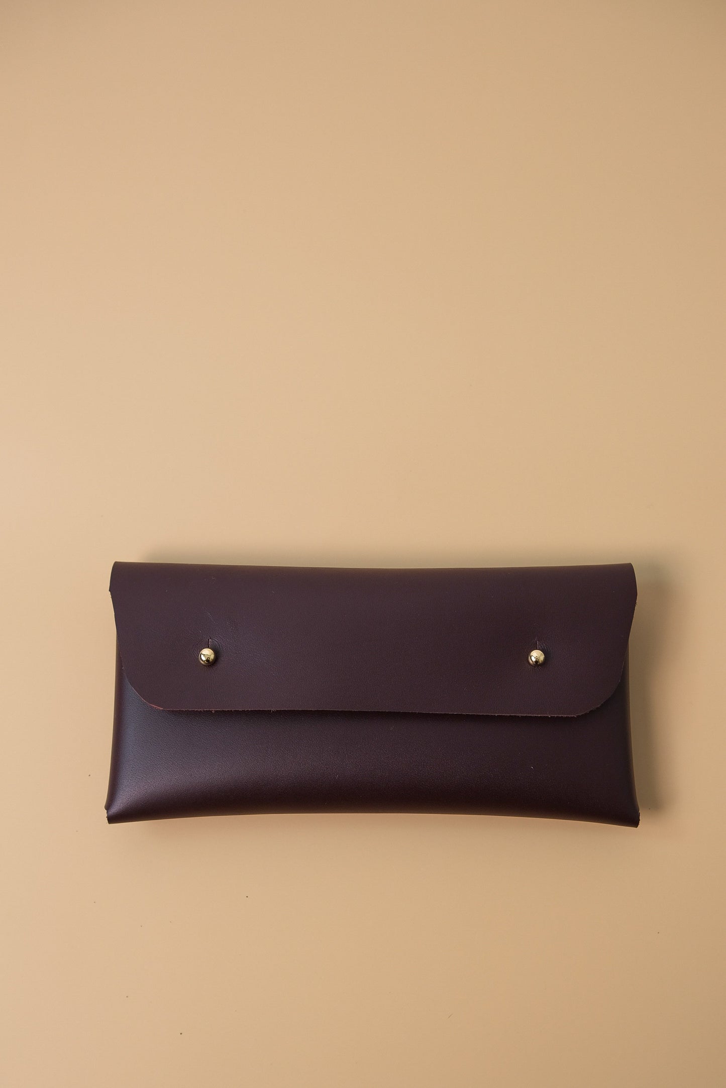 Dark brown leather clutch with gold studs on a beige background