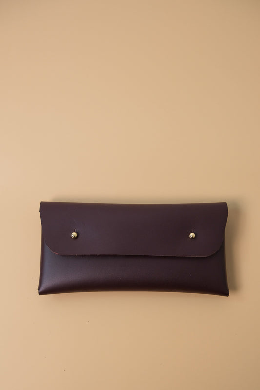 Dark brown leather clutch with gold studs on a beige background