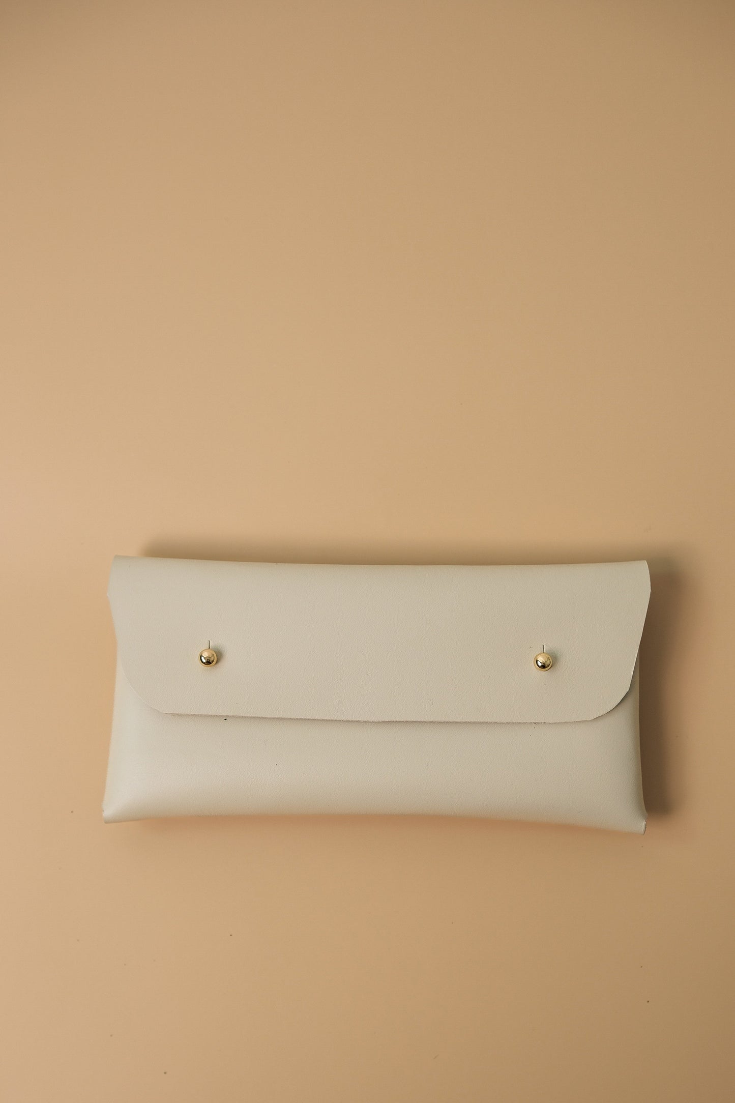 White leather clutch with gold studs on a beige background
