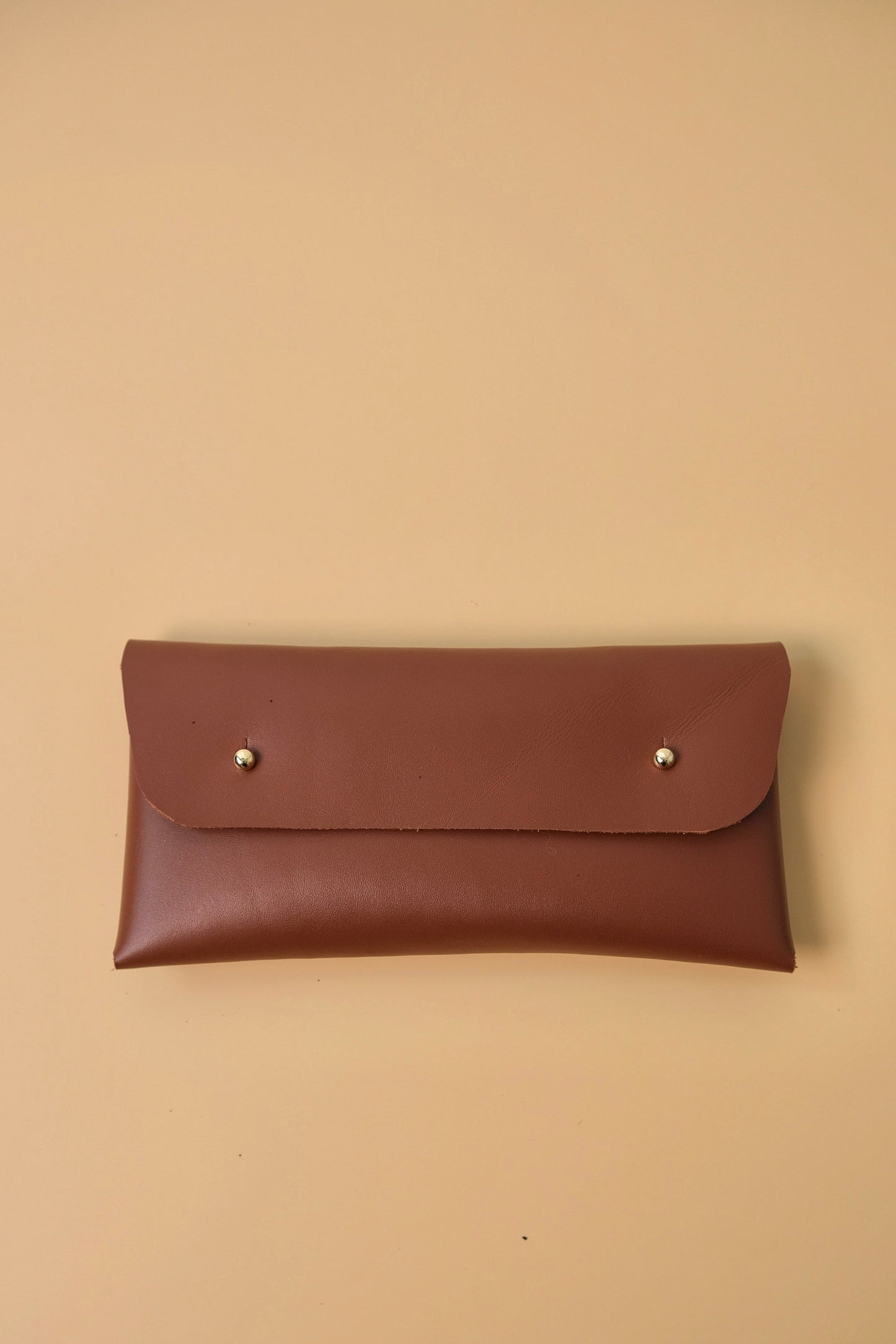 Brown leather pouch with silver studs on a beige background